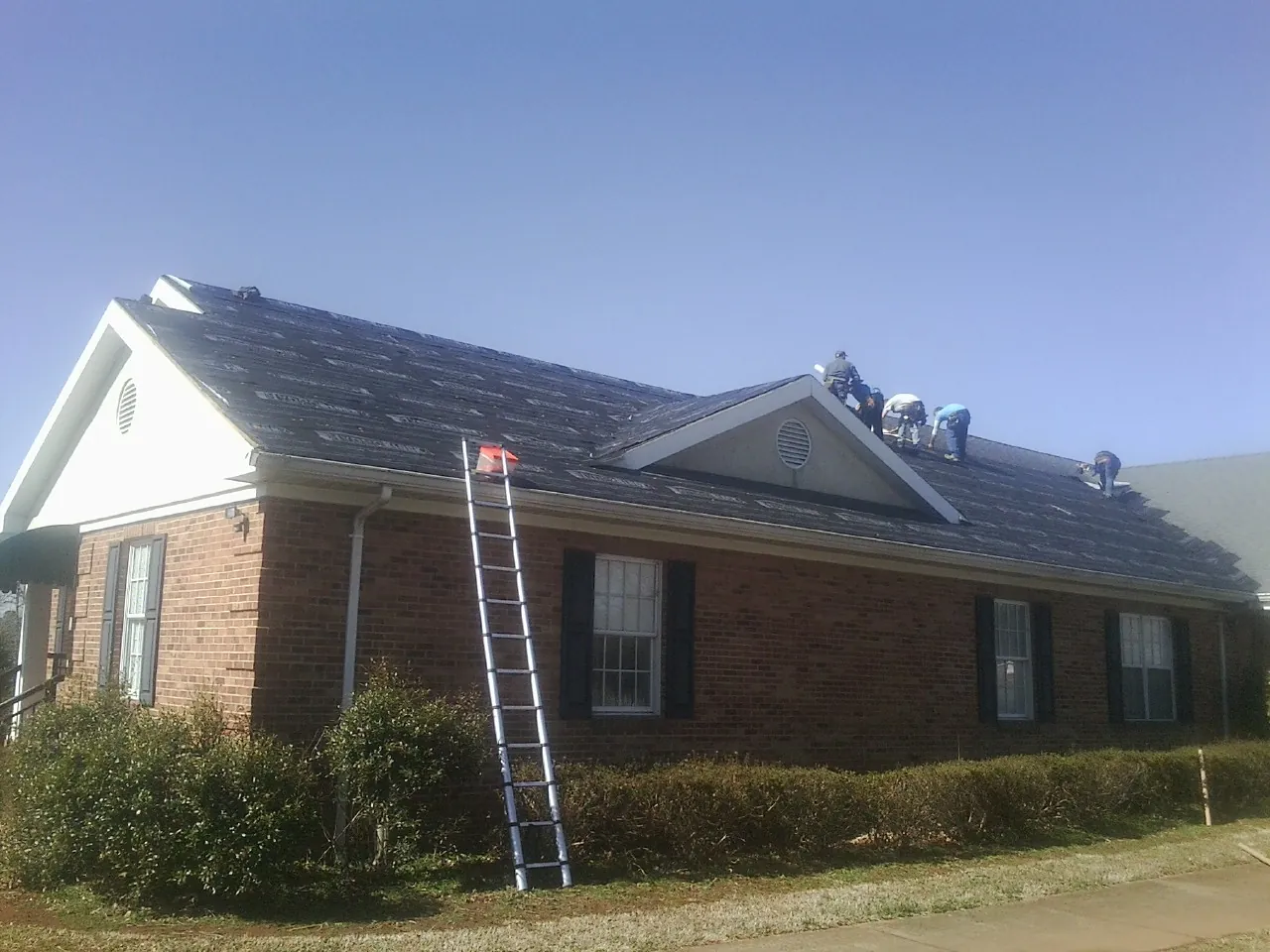 Crew tearing shingles off a brick ranch roof with a ladder set — Emergency Roof Repair work by our crew in Solomon