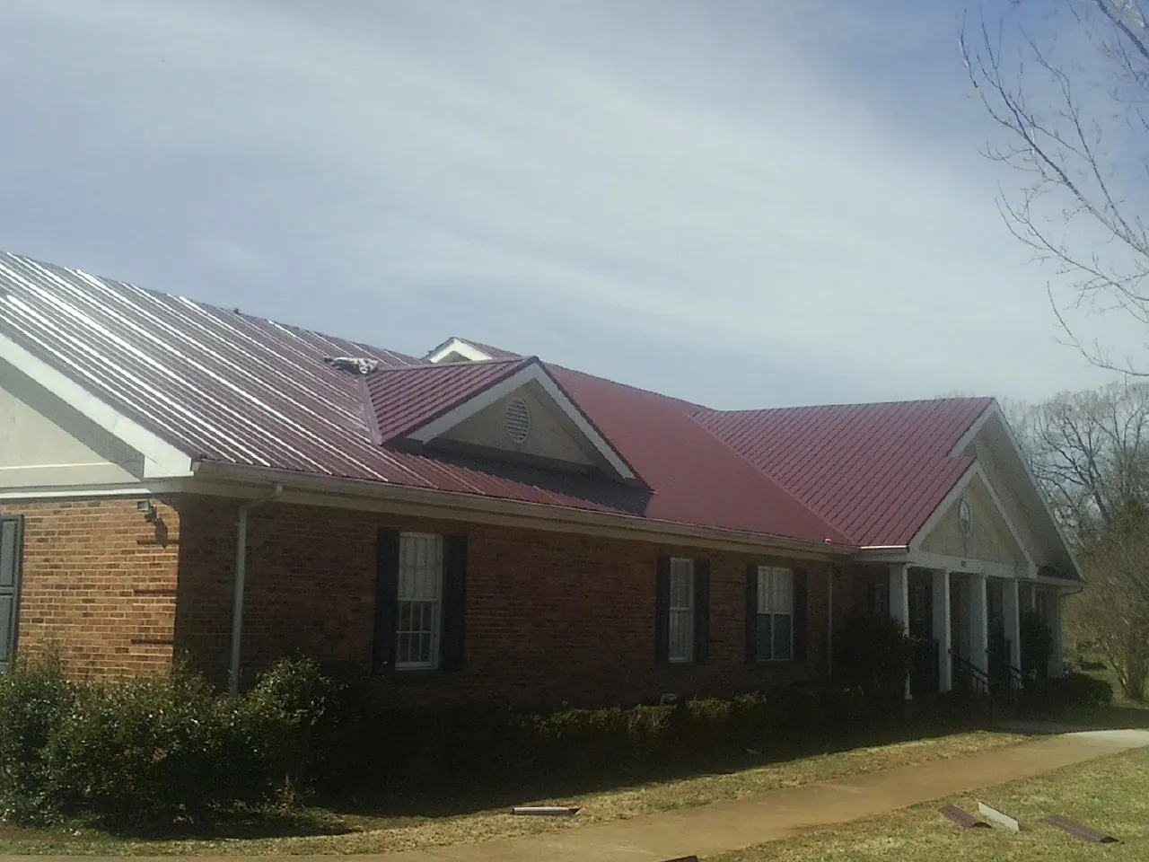 Red metal roof with gabled entries on a long brick building, from a Hail Damage Roof Repair job in Solomon