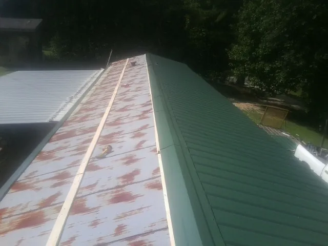 Old rusted panels beside newly installed green metal roofing — Wind Damage Roof Repair by Roofing Brothers in Solomon