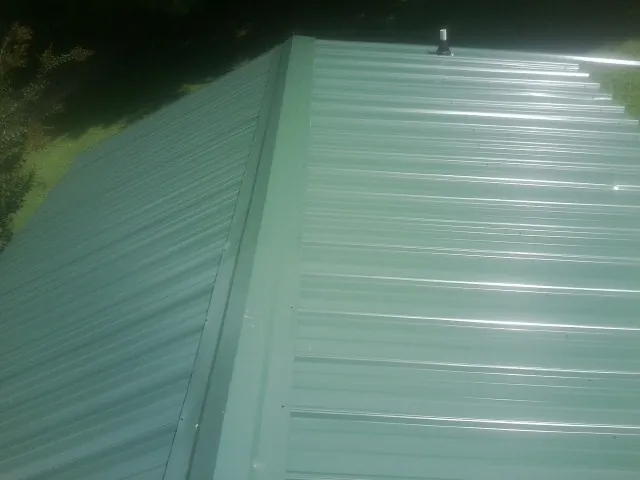 New green metal panels meeting at the ridge of a roof — Flat Roof Repair work by our crew in Solomon