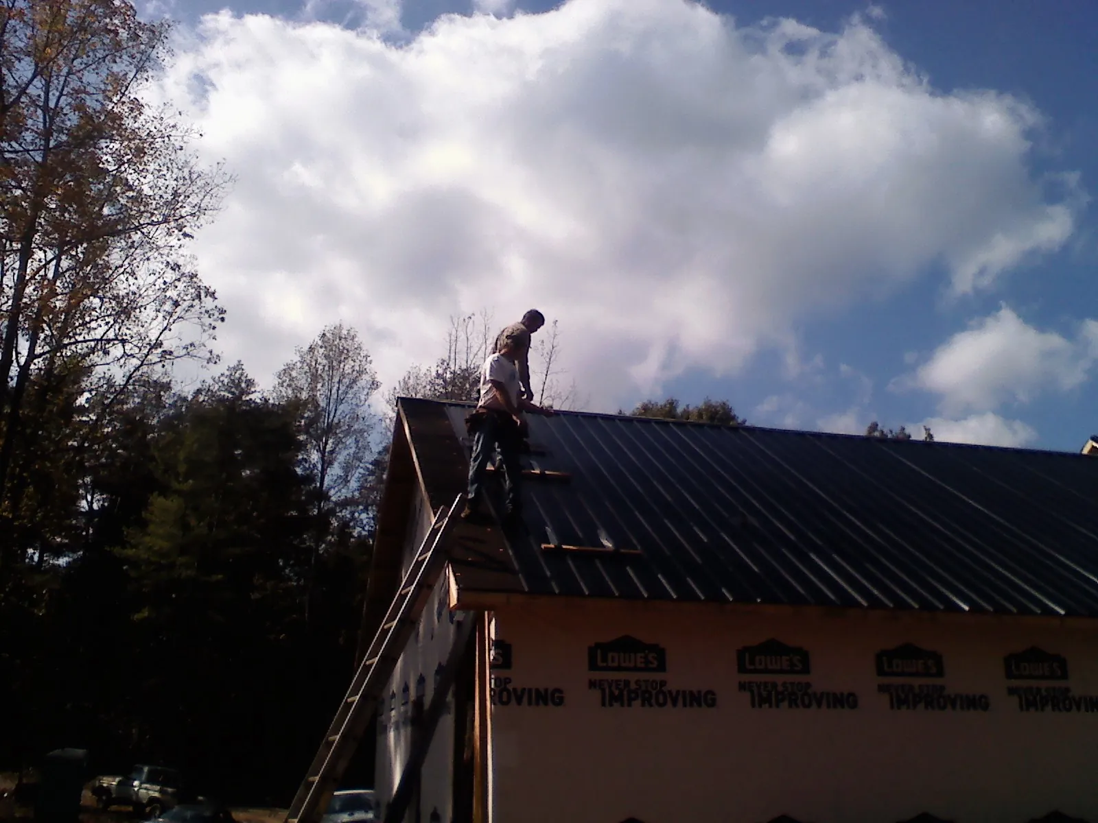 Roofer fastening dark metal panels high against a cloudy sky, from a Roof Inspection job in Solomon