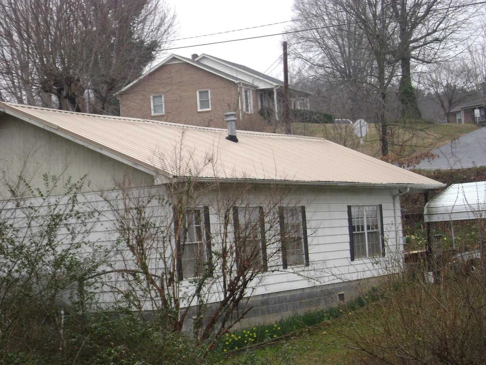 Tan metal roof on a white sided house set into a hillside — Commercial Roofing by Roofing Brothers in Solomon